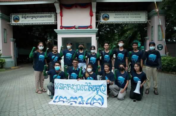 A group of 15 young people standing and kneeling in front of the Ministry of Tourism building, holding a banner to the camera. It reads “Koh Kong Island must become a marine national park”