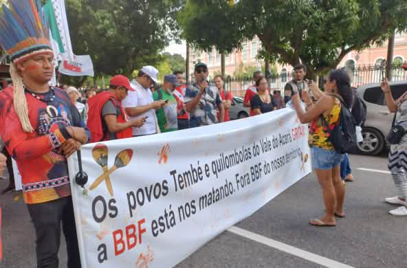 A group of indigenous people protest with a large banner on a street in a town: the banner reads: ‘The Tembé and Quilombola peoples of the Acará Valley are crying out. BBF is killing us. BBF out of our territory