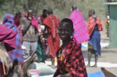 Maasai women and men in colorful cloths at a market, a woman looks at the camera