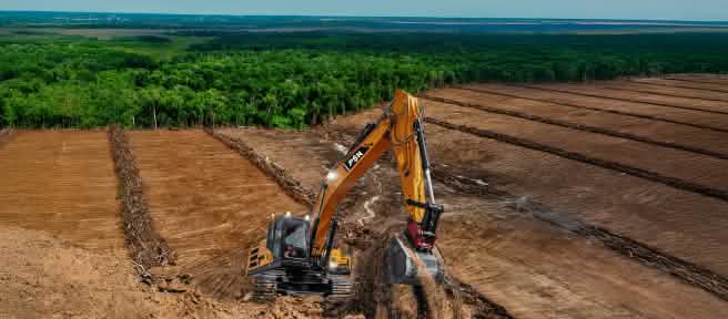 Excavator on deforested land – the forest in the background is threatened