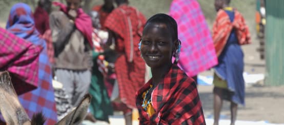 Maasai women and men in colorful cloths at a market, a woman looks at the camera