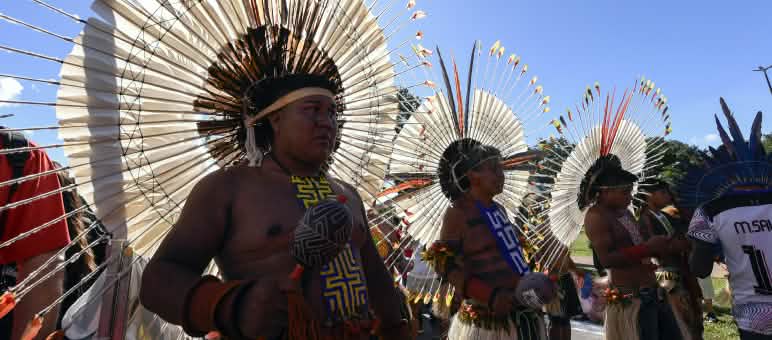 Three Indigenous people wearing large round feather headdresses