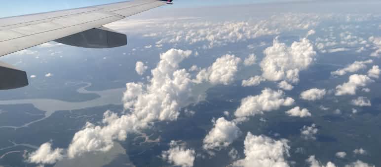 "Sustainable" air travel with carbon credits from offsetting projects in the rainforest? View of clouds, rivers and rainforest seen from an airliner, with the wing at the top of the frame