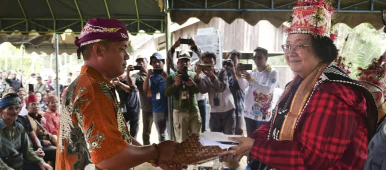 Village chief Willem Hengki presents the petition to Minister Siti Nurbaya Bakar Willem Hengki and Siti Nurbaya, with numerous photographers in the background