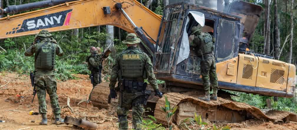 Armed police officers of the environmental agency IBAMA disable an excavator used for illegal gold mining in the rainforest of the Indigenous Munduruku A group of men in camouflage suits from the environmental agency IBAMA disables a yellow excavator in the rainforest