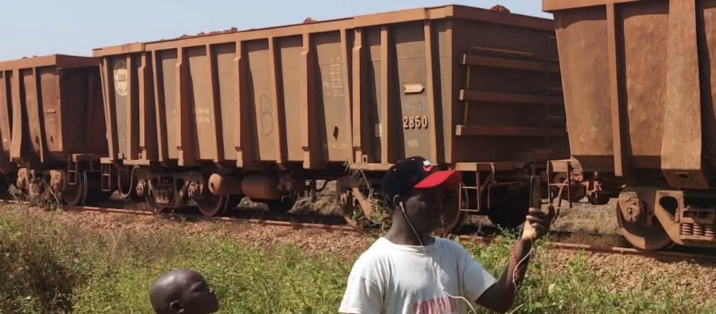 Bauxite from Guinea on the way to the port A freight train, a boy and a man in the foreground