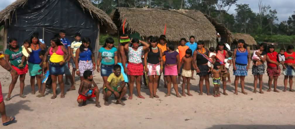 The Ka'apor have preserved their traditional way of life in their villages. Indigenous Ka'apor standing in a double row in front of two huts in the forest