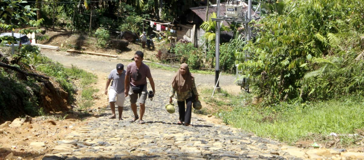 Three people on a paved road in a village in the forest