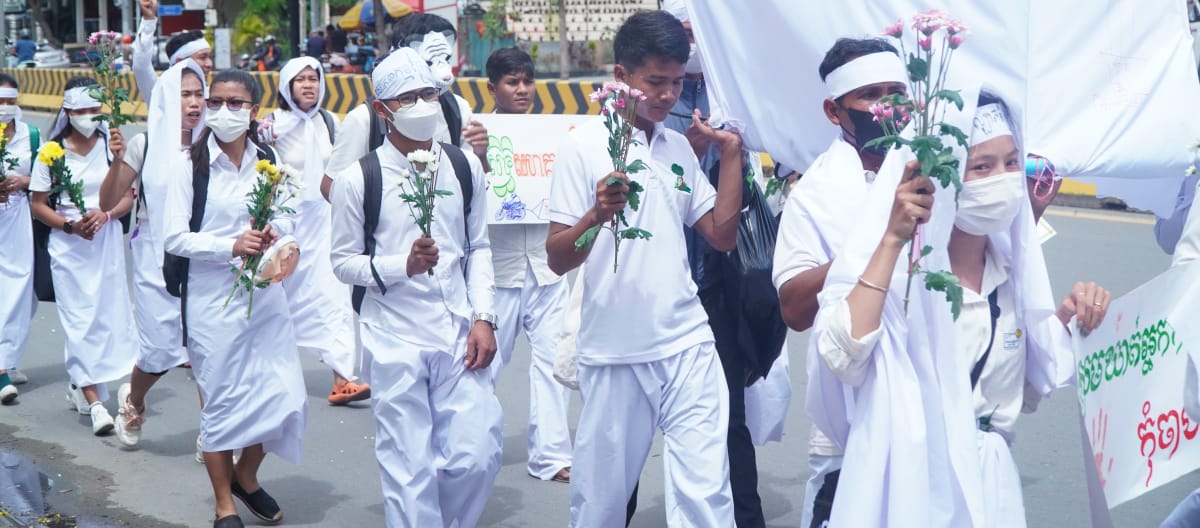 Young people dressed in white walk through a street in Phnom Penh with flowers in their hands