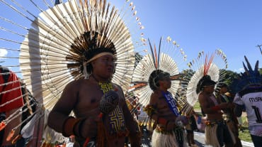 Three Indigenous people wearing large round feather headdresses