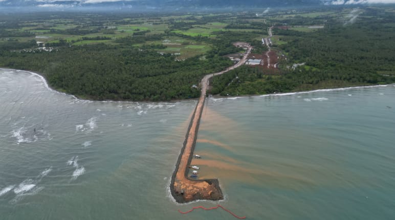 A brown jetty leads from the nickel mine in the rainforest out to sea. Aerial view