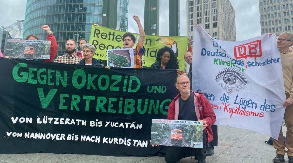 A group of people protesting with large, colorful banners in front of three office buildings