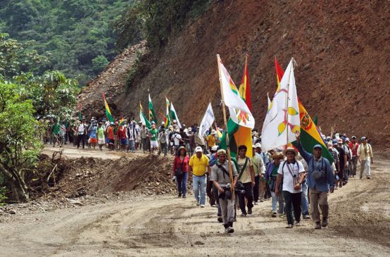 Indians on a protest march with flags in their hands walking up a gravel road