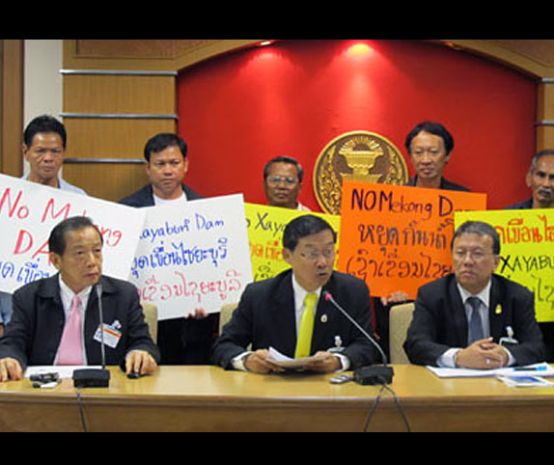 Politicians sitting at a table: Protesters behind them