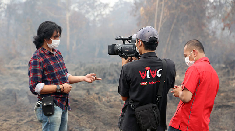 A man being interviewed with a burning rainforest in the background